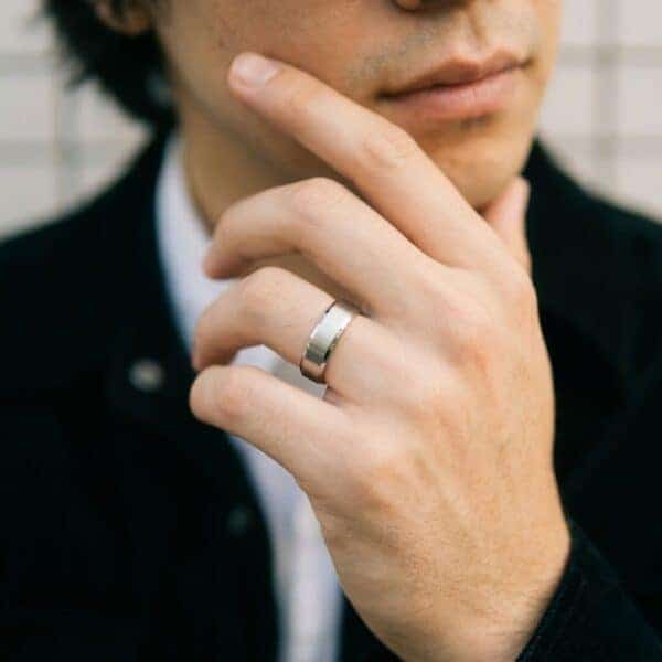 With his chin resting on his hand, the man holds a thoughtful pose. The mans hand is at the centre of the image. On his wedding finger, he has a brushed silver titanium ring. The edges are polished silver titanium and are bevelled. The interior of the ring is polished blue.