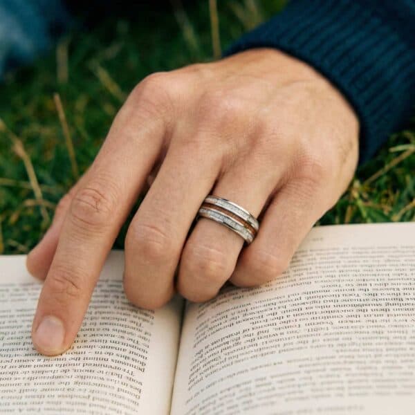 Reading his favourite book, a man points to the words as he reads. He is wearing a tungsten ring that features grooves of natural wood and antler.