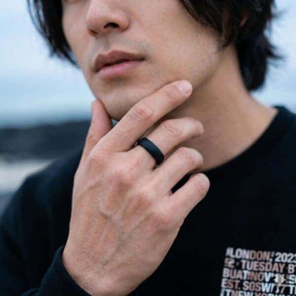 Wearing a black t-shirt and with black hair, a man brings his hand to his chin in a very thoughtful pose. On his middle finger, he wears a black silicone ring. The ring is slightly domed.