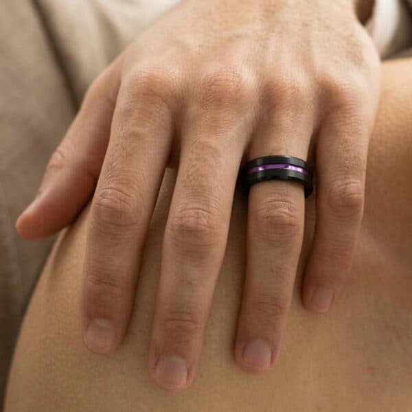 A close up image of a mans hand resting on his partners shoulder. The man is wearing a black tungsten ring that has a vivid groove of purple that runs through the centre of the ring.
