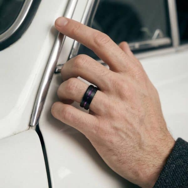 A man reaches his hand out to open the door of the white car. The camera is zoomed in to the hand. It is a mans hand and he is wearing a tungsten ring - a black ring that features a purple groove and interior.