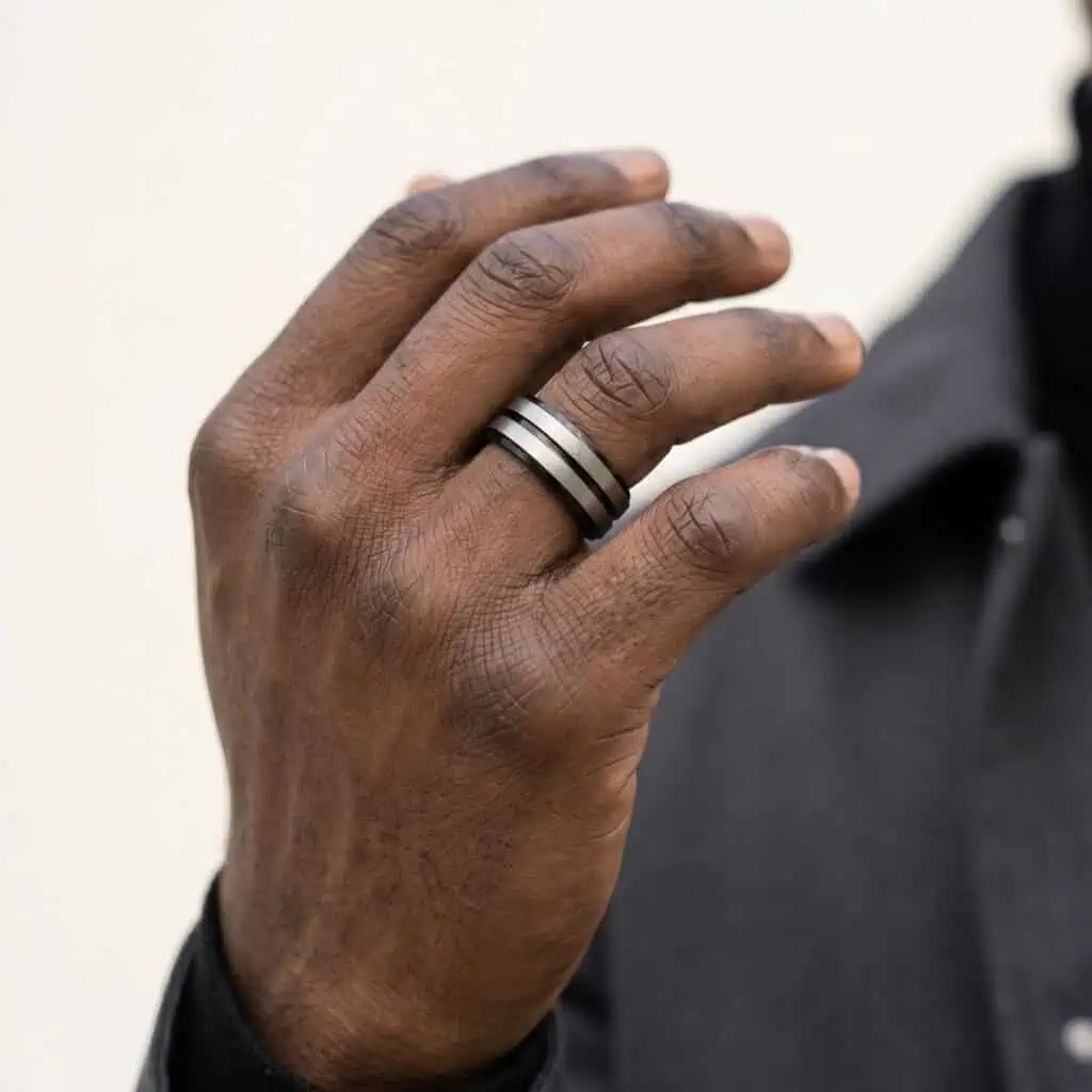 Close-up of man’s hand wearing polished black titanium ring with raised brushed silver sections