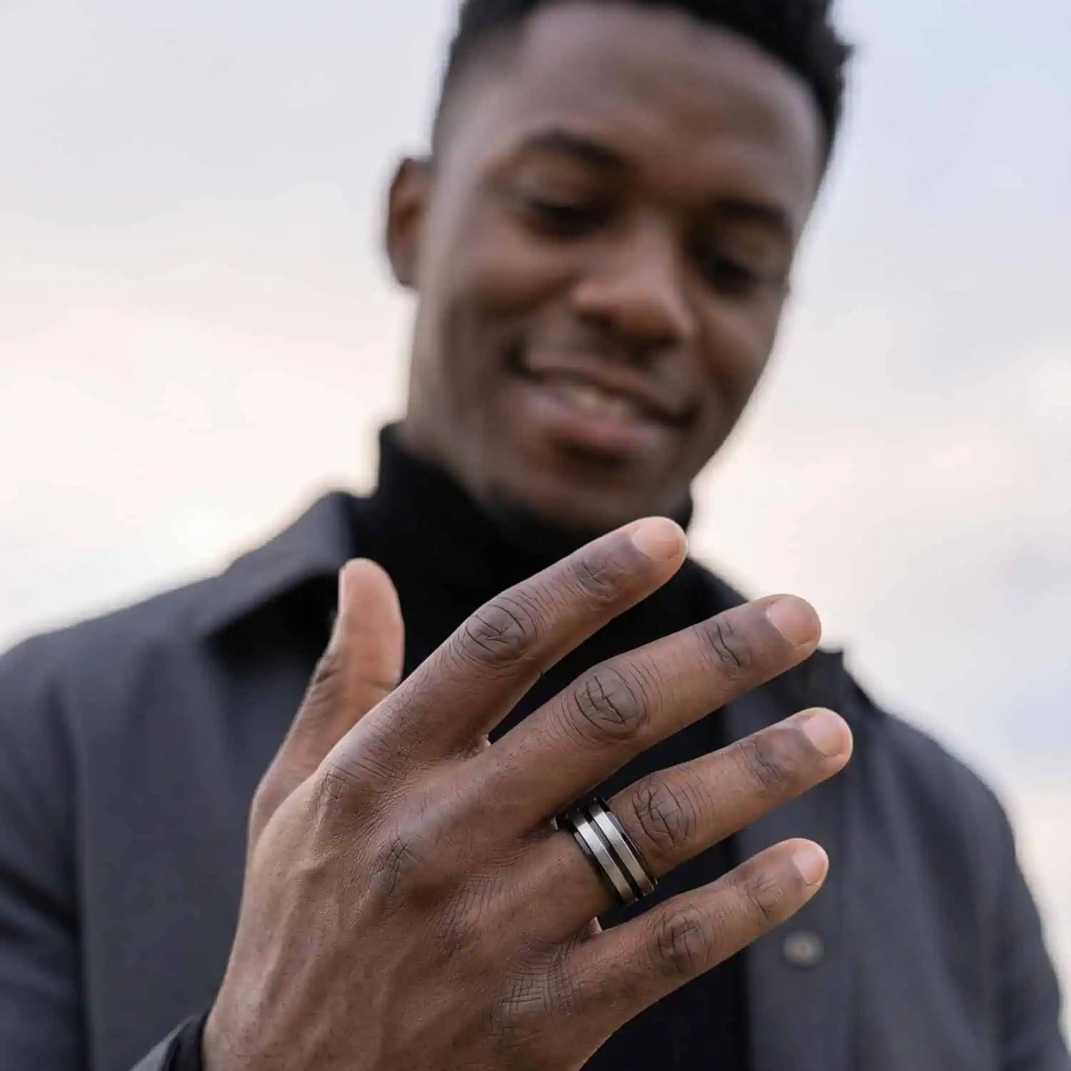 Man in black jacket smiling with hand forward wearing polished black titanium ring with brushed silver sections