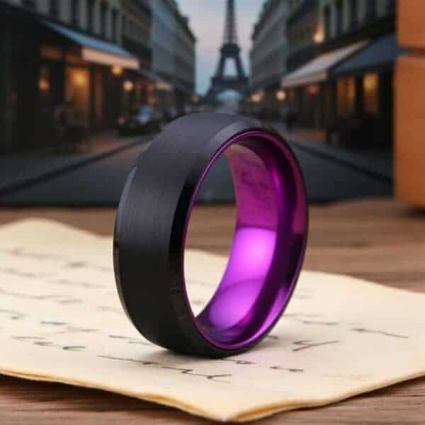 With the streets of Paris in the background, a ring stands upright on some sheets of paper. The ring is a black tungsten ring with a bright purple inside.