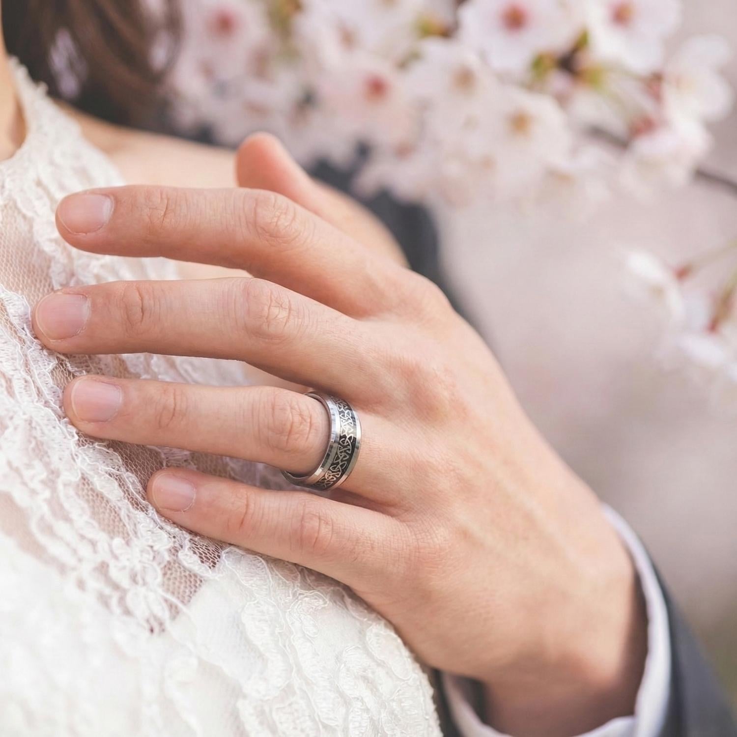A close up image on a man's hand who is embracing the bride. He is wearing his new wedding ring which is a silver tungsten band with an intricate pattern inlay made of carbon fibre.