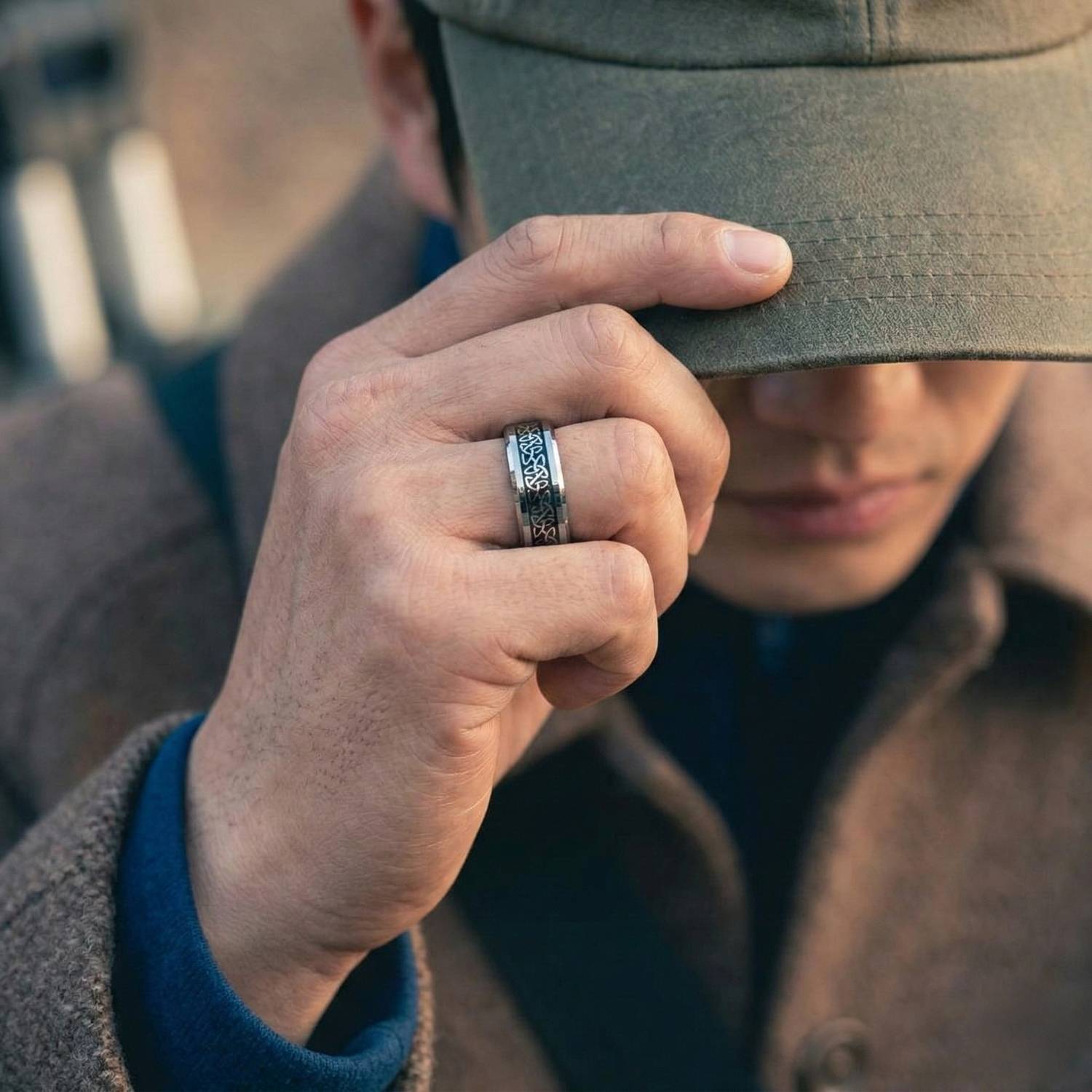 Sheltering from the weather, a man in an overcoat pulls his hat low over his face. On his hand is a silver tungsten ring that features a celtic knot pattern made with carbon fibre.