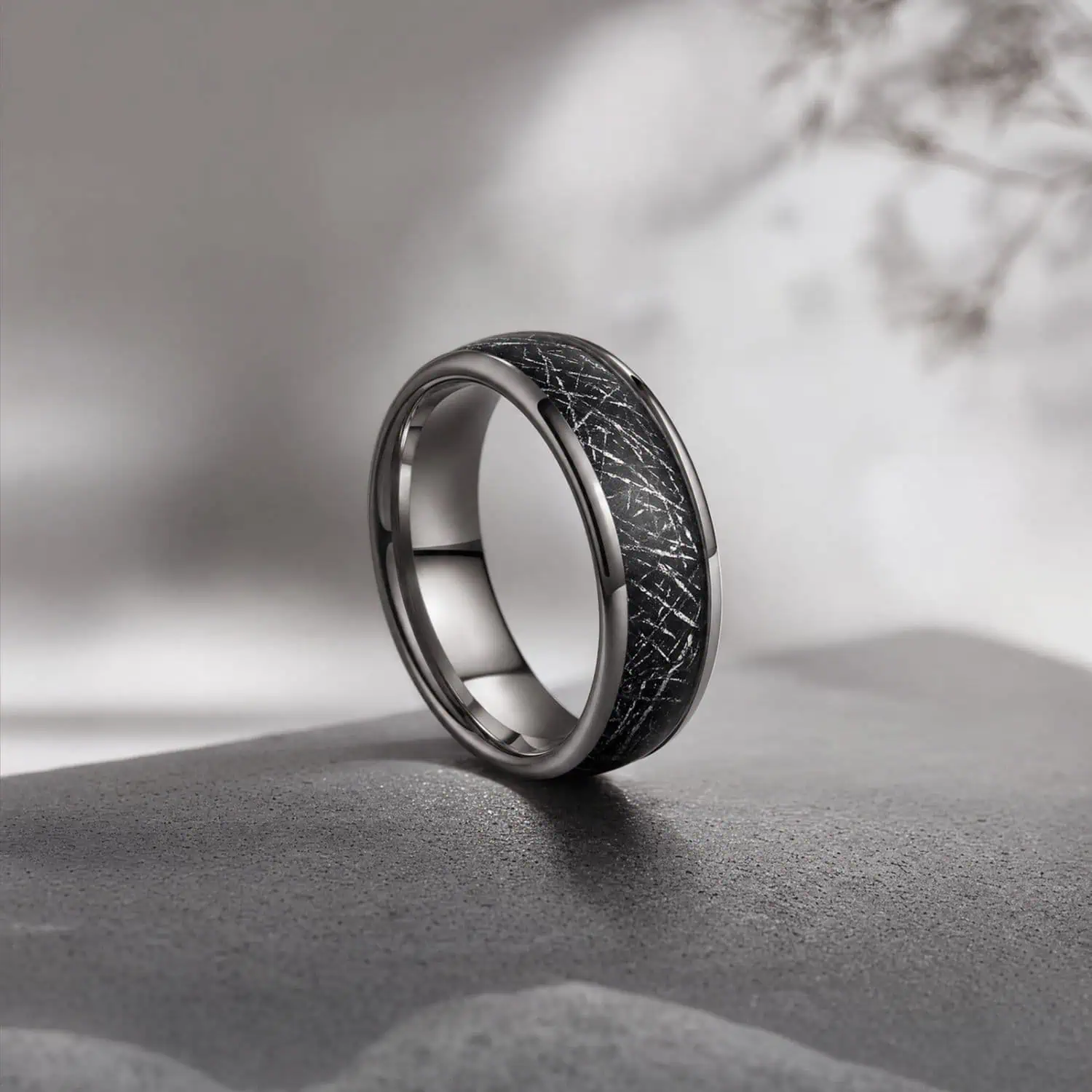 8mm silver tungsten ring standing upright on a concrete-style surface against a minimalist grey and white background, showcasing its black faux meteorite inlay.