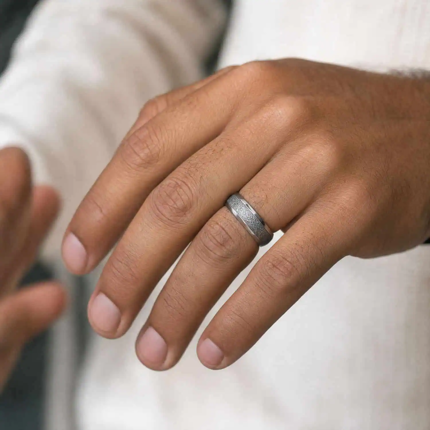 Close-up of a man's outstretched hand displaying his polished silver tungsten wedding ring with a black and silver faux meteorite pattern through the centre.