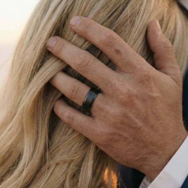 A women leans towards her partner while his hand rests on the back of her head. On his wedding finger, he wears a black ceramic ring.