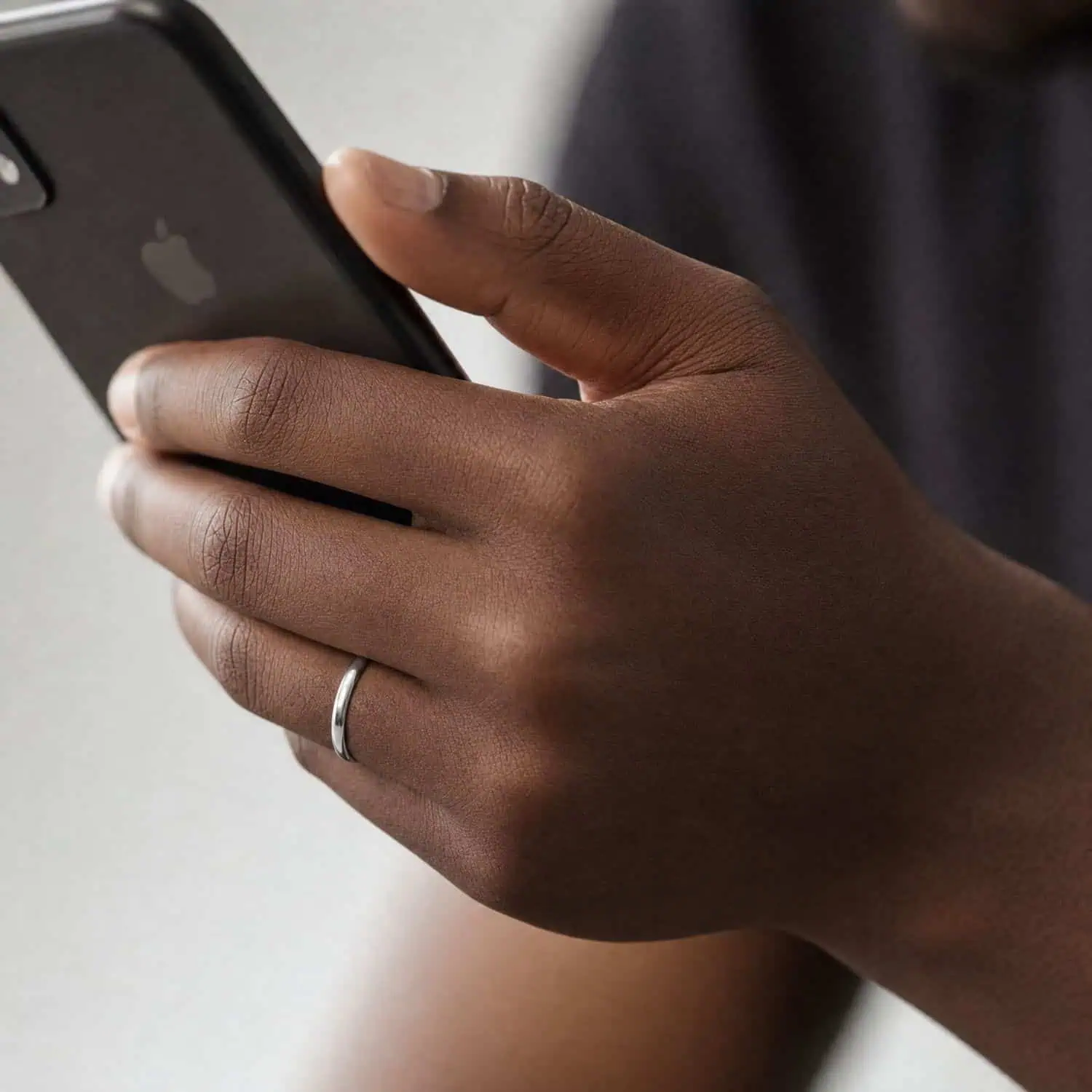 Close-up of a man's hand holding his mobile phone while wearing a slim 4mm polished silver tungsten carbide ring on his wedding finger.