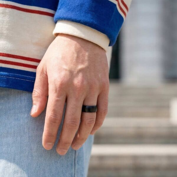 A close up image of a mans hand. You can see the blue and red stripes of his top. On his hand, he is wearing a brushed black ring. The ring is made with ceramic.