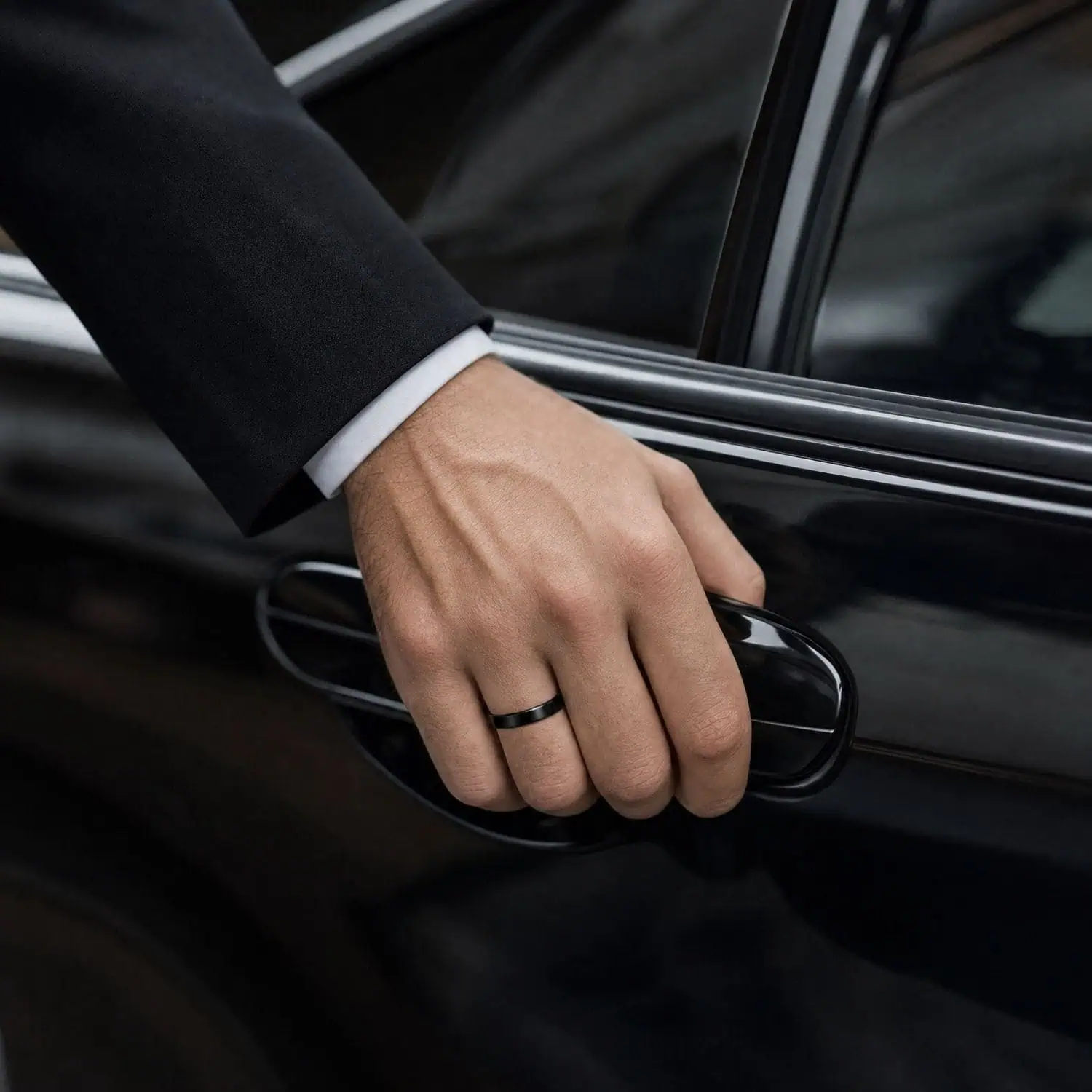 Groom wearing a polished black ceramic wedding ring while opening the door of a shiny black wedding car.