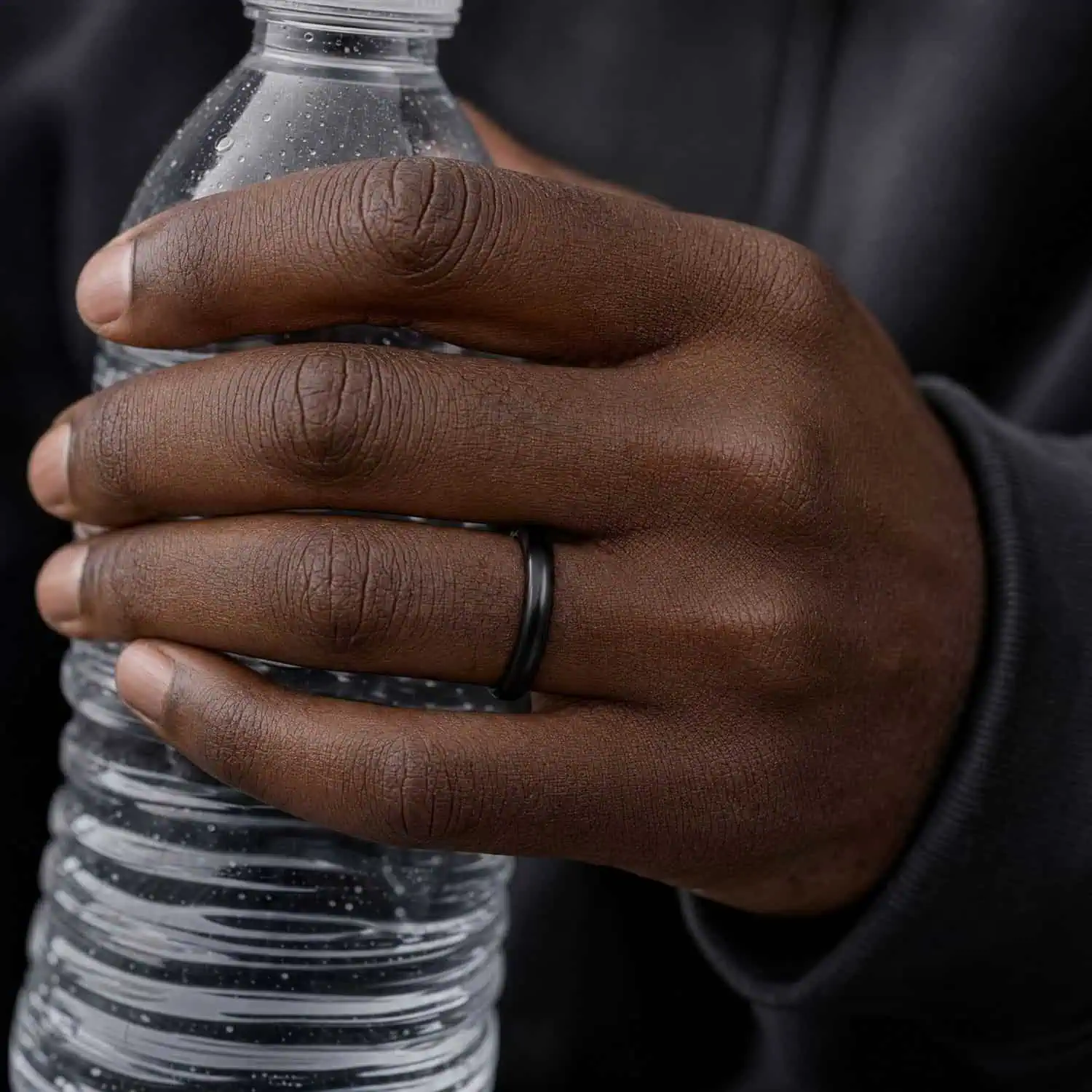 Close-up of a man's hand holding a water bottle while wearing a slim 4mm black ceramic ring with a smooth polished finish.