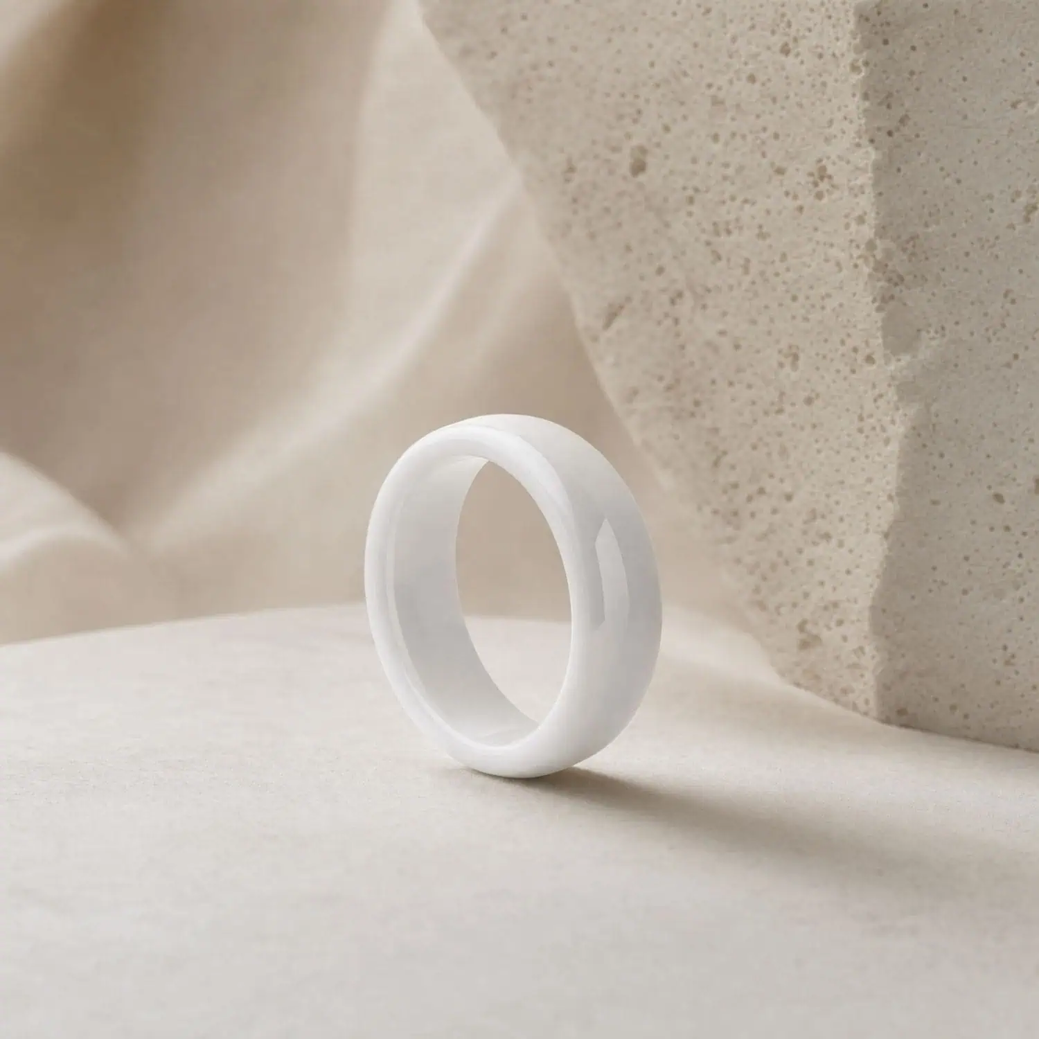 Bright white polished ring standing upright on a white surface beside a natural white rock, highlighting its smooth finish and minimalist band design.