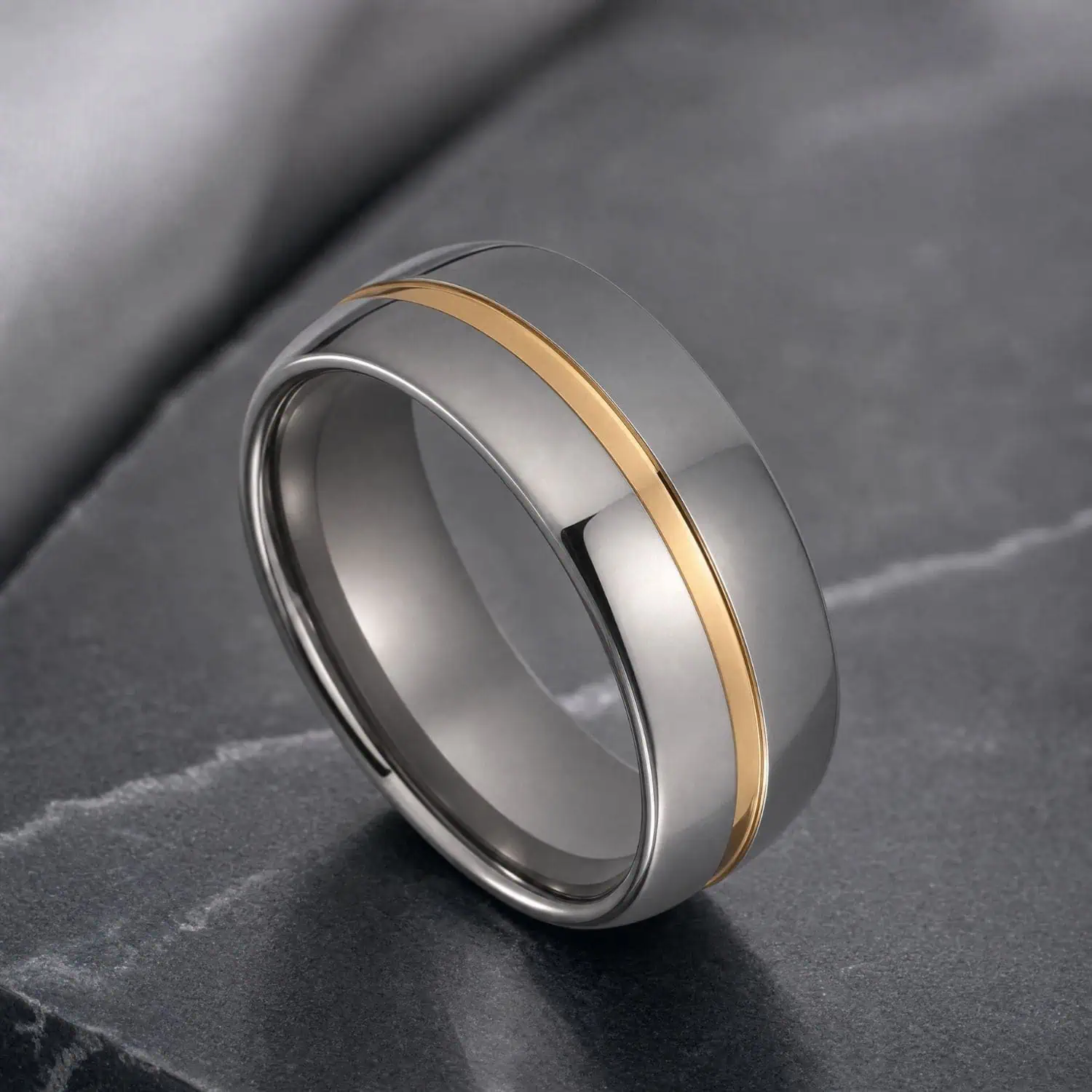 Silver tungsten ring with a polished gold groove through the centre, displayed in close detail on dark grey marble.