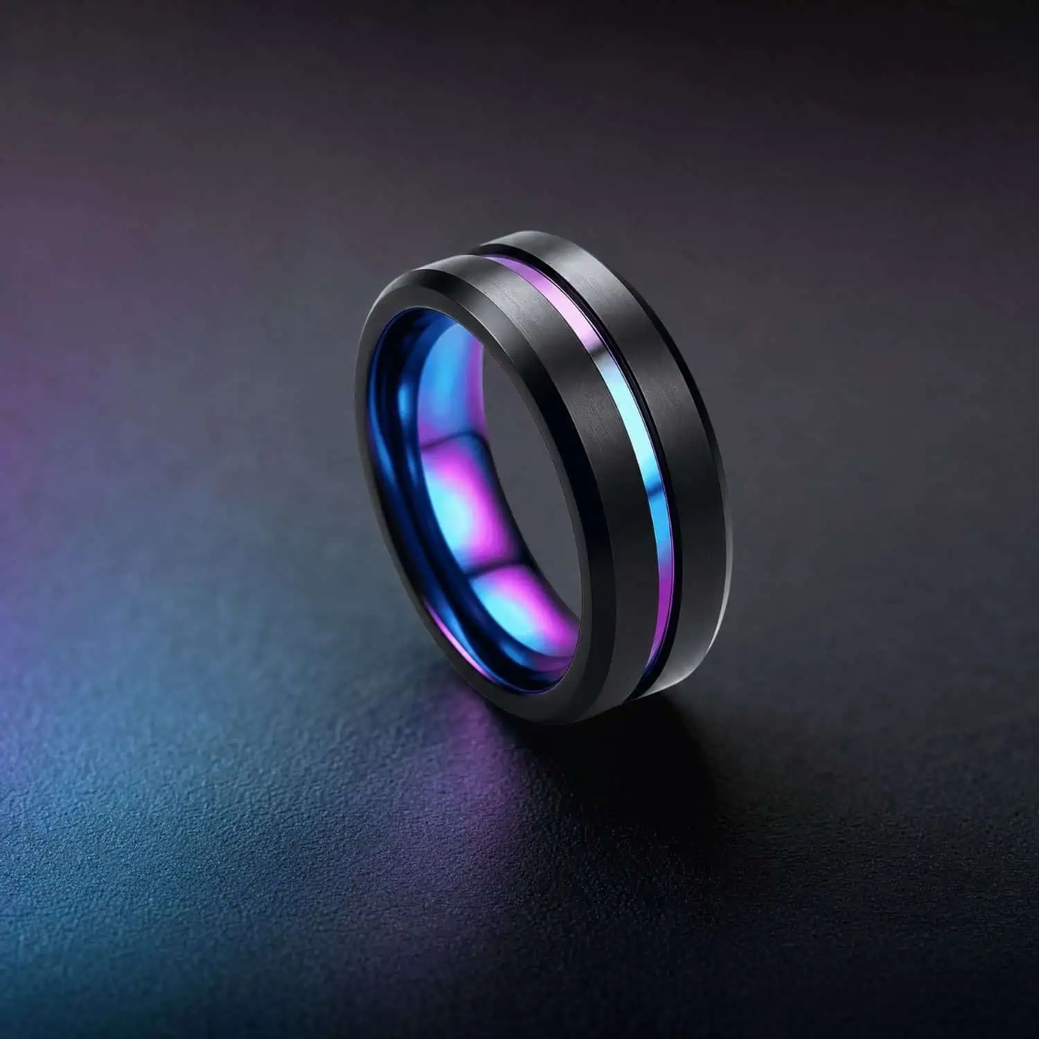 Iridescent tungsten ring standing upright on a black surface with subtle multicoloured reflections, highlighting its dark exterior and shimmering rainbow centre groove.