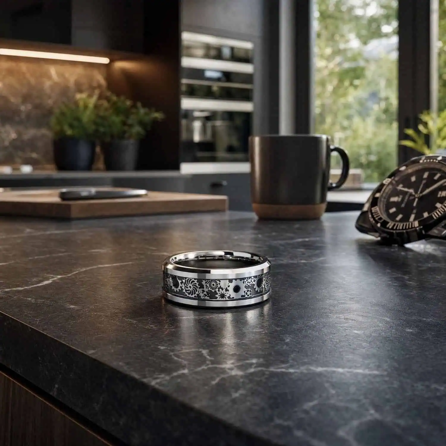 Men's silver tungsten ring with a black carbon fibre and gear inlay displayed on a black marble worktop beside a watch and mug.