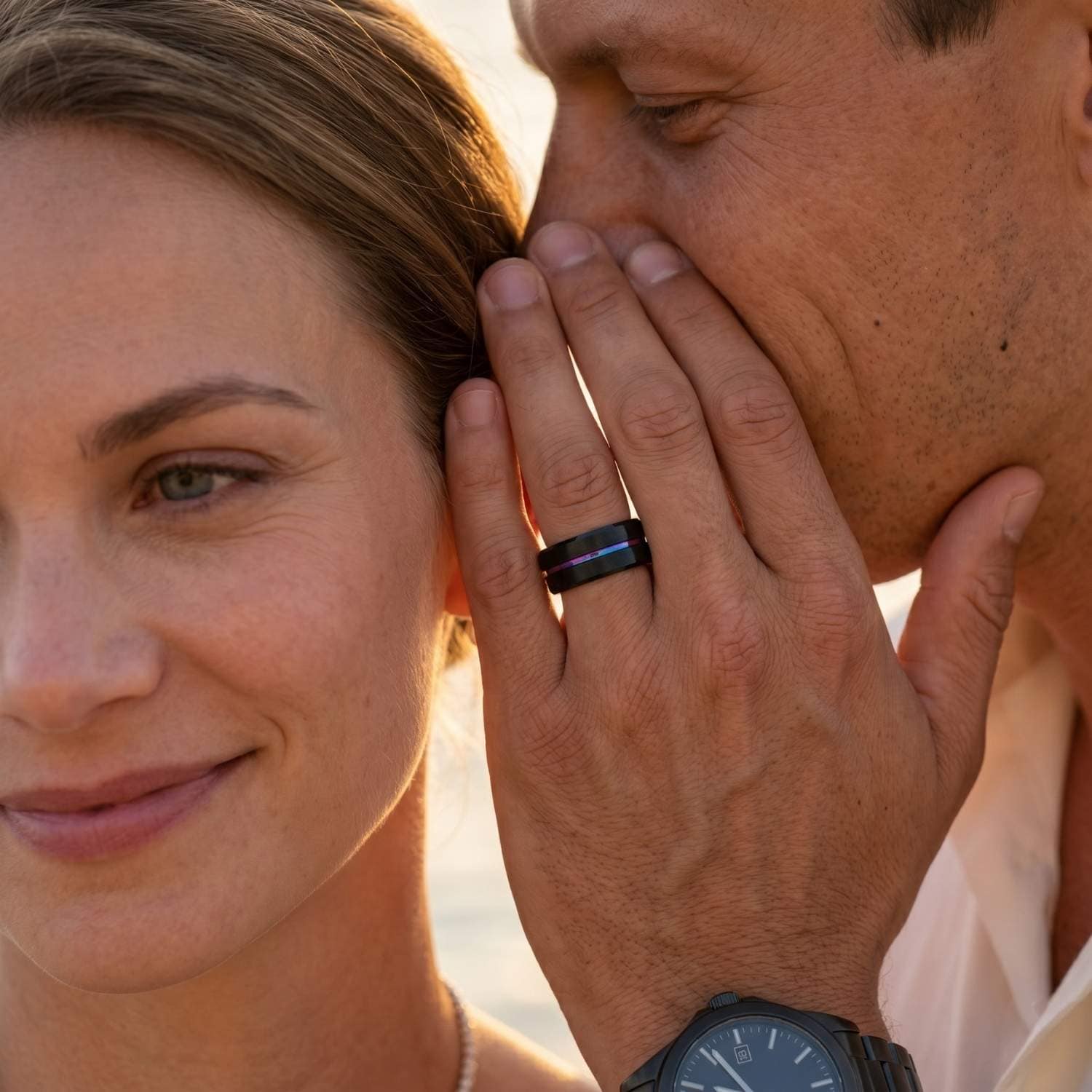 Bridal couple sharing a quiet moment as the man wears the Unity black tungsten wedding band with an iridescent rainbow groove while whispering to his partner.
