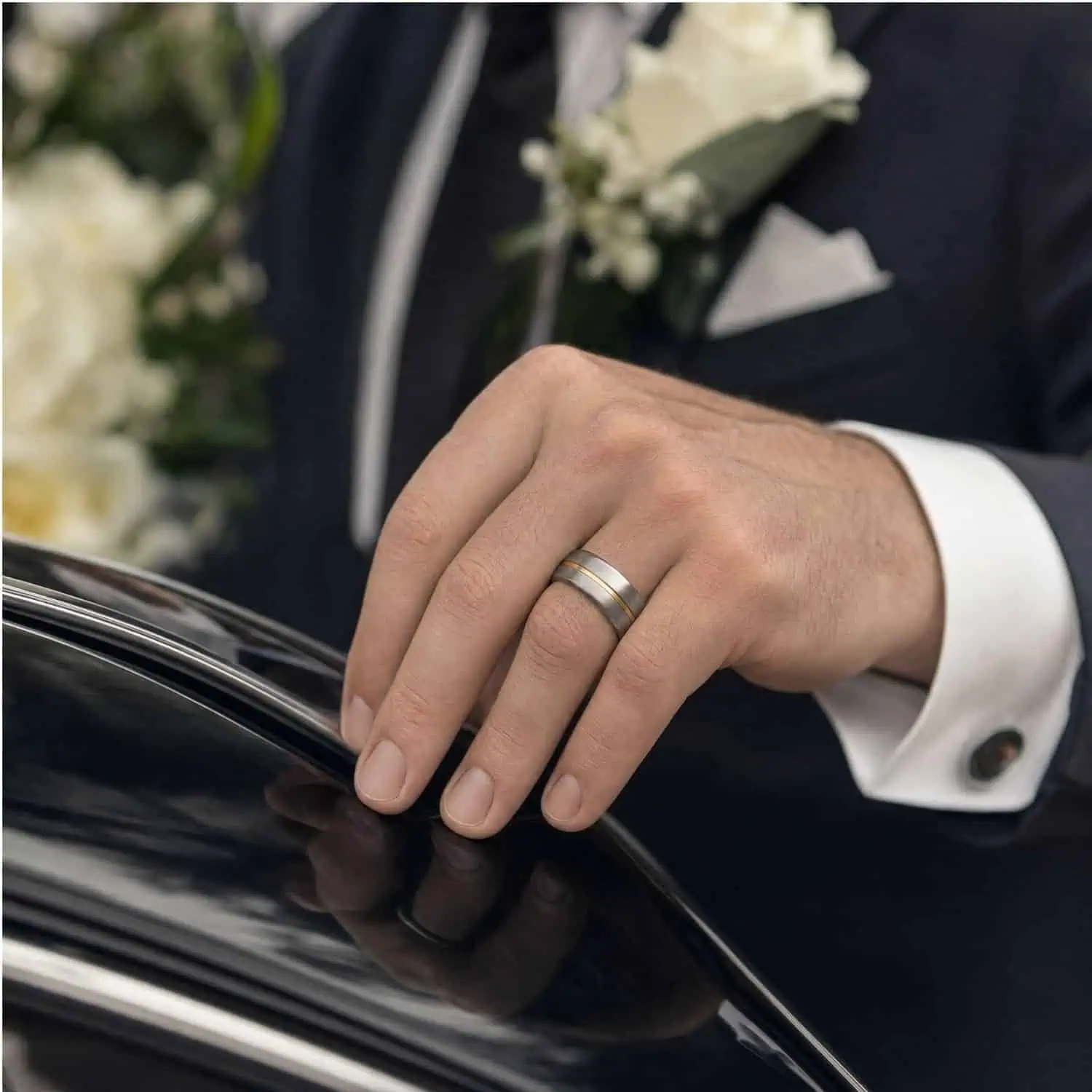 Groom wearing a polished silver and gold tungsten wedding band with his hand resting on a black wedding car.