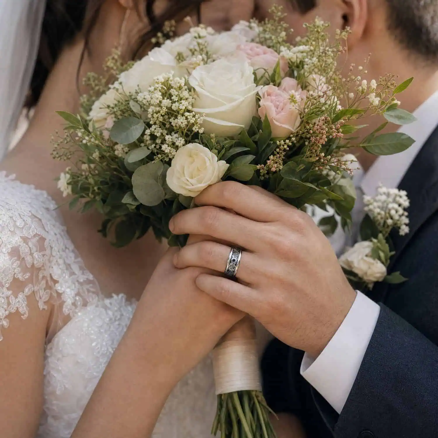 Bride and groom sharing a quiet moment behind their wedding bouquet, with the groom wearing a silver tungsten wedding ring featuring black carbon fibre and gear detailing.