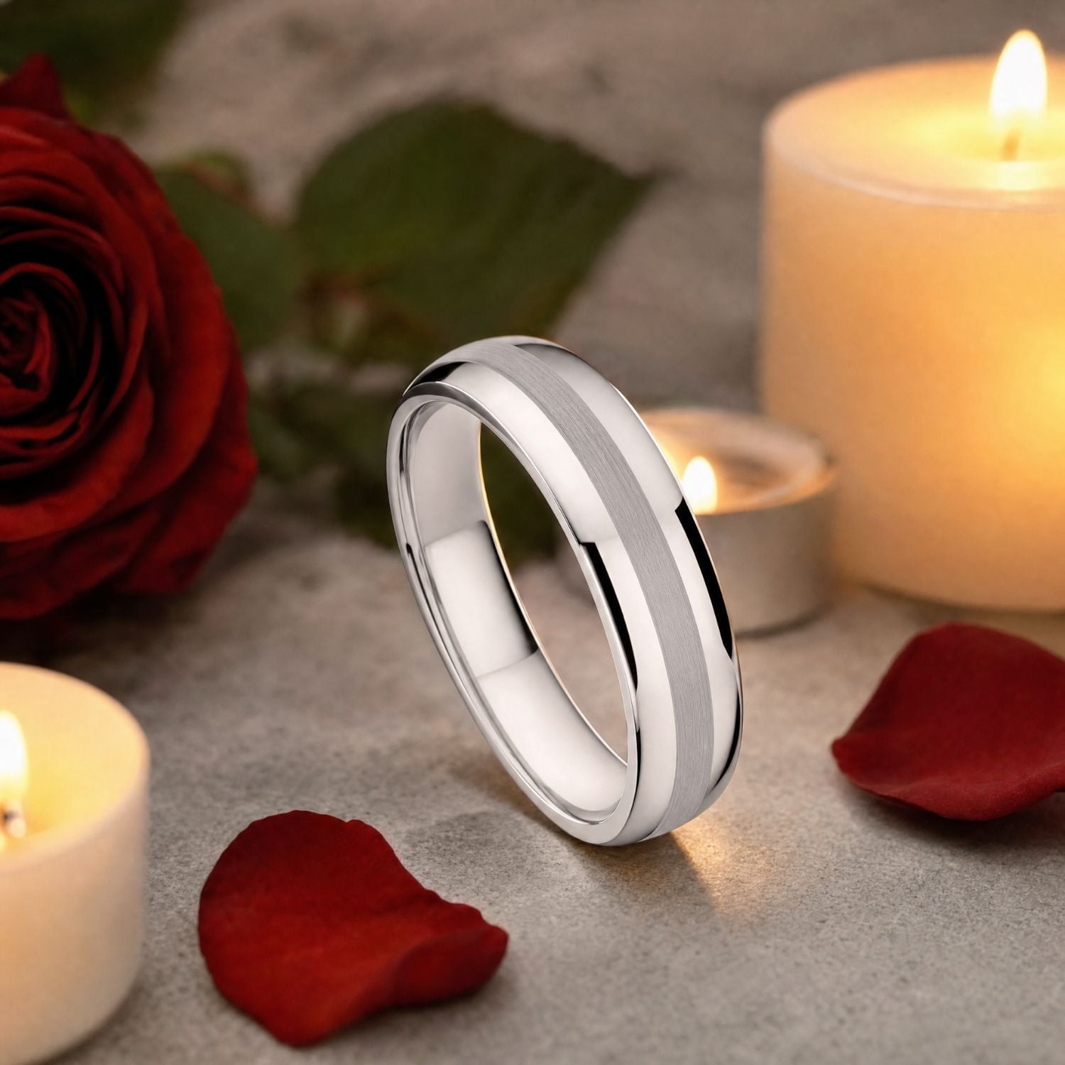 The Knight silver tungsten wedding band standing upright among red rose petals with a red rose and two burning white candles, showcasing its brushed centre and polished sides.