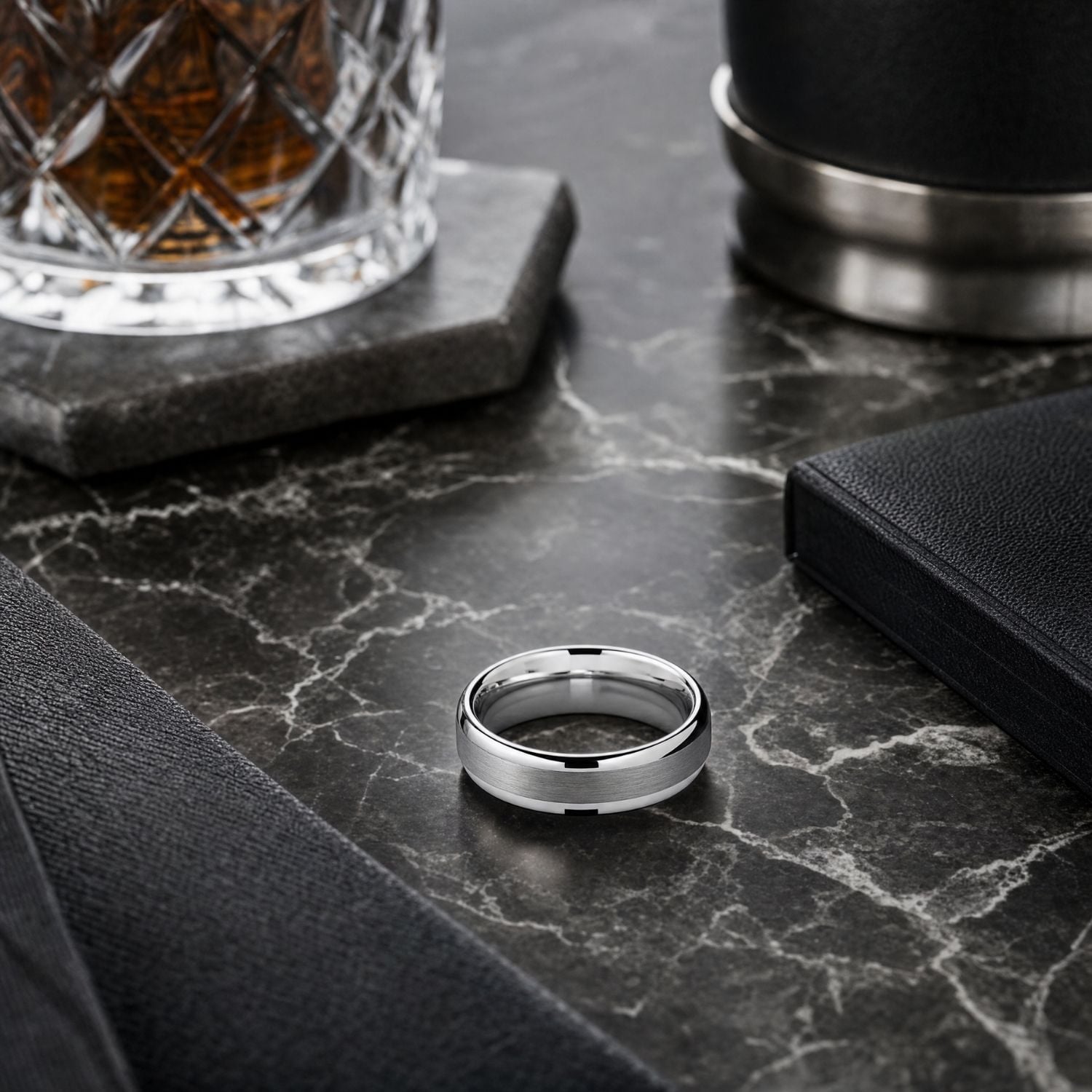 The Knight silver tungsten ring displayed on a marble coffee table beside a tumbler of whiskey on a marble coaster.