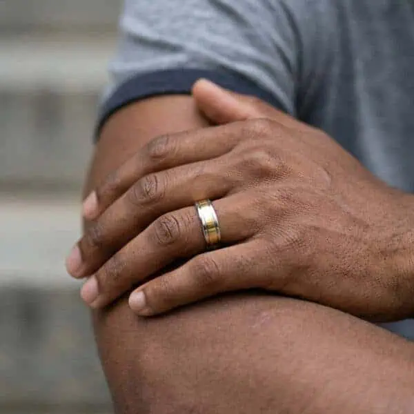 A close up image of a mans arm and hand. With his arms crossed, you can see that the man is wearing a gold and silver tungsten ring.