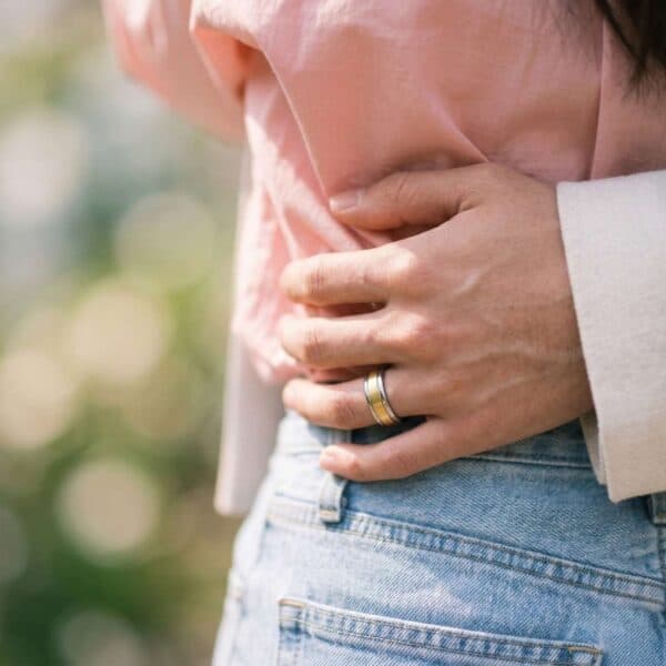 A man has his arm around the waist of his partner. The woman is wearing a pink shirt. The man has a gold and silver tungsten ring on his finger.