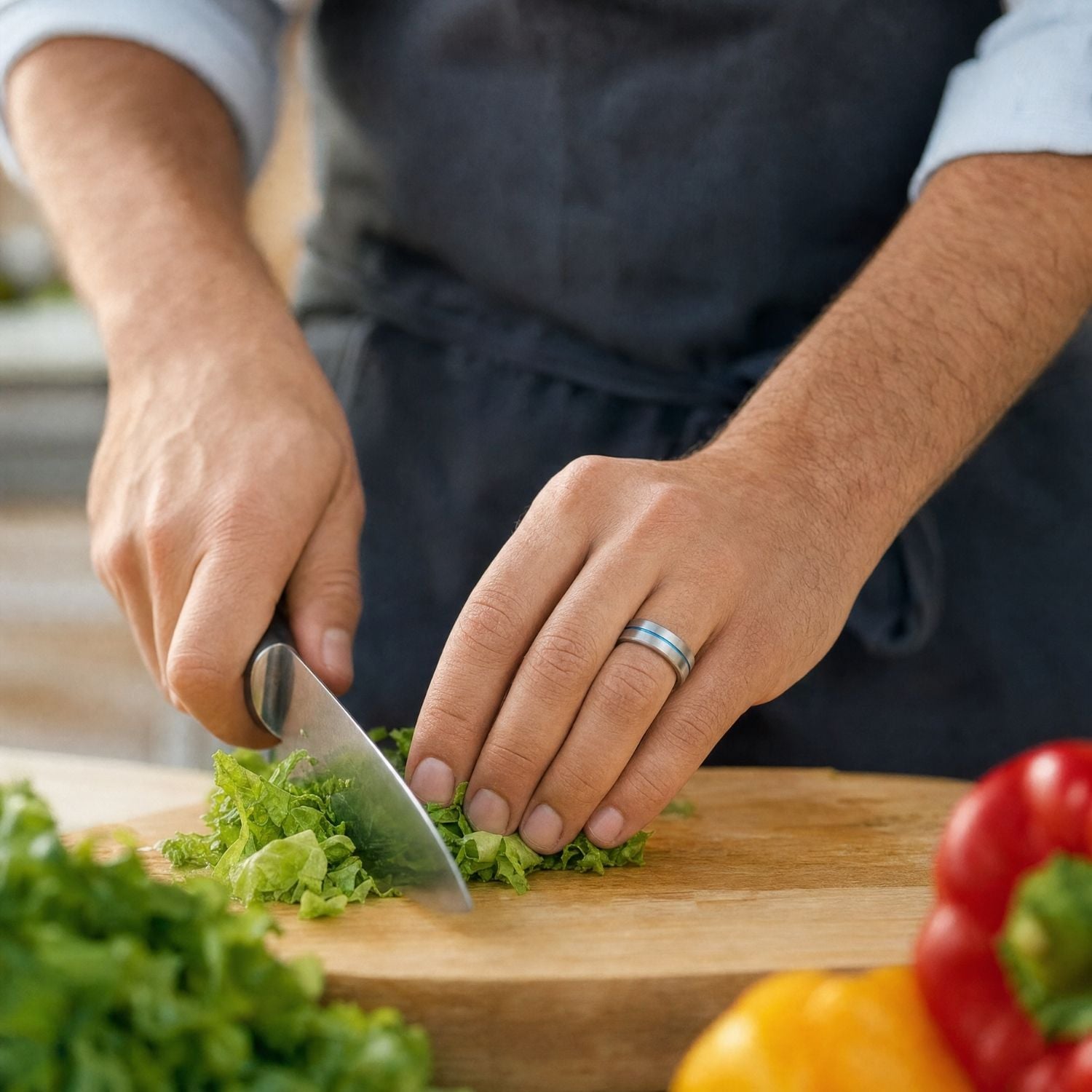 Close-up of a man's hand chopping lettuce while wearing the Negotiator brushed silver tungsten ring with a polished blue groove.