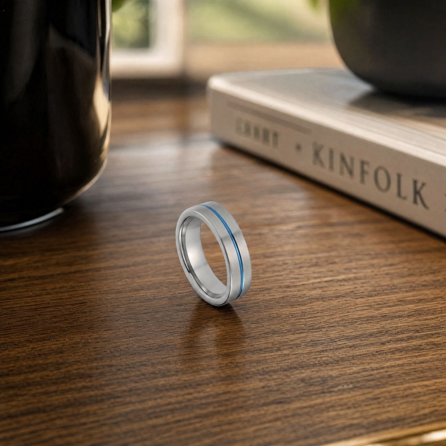Negotiator men's tungsten ring standing upright on a wooden desk, showcasing its brushed silver finish and polished blue centre groove.