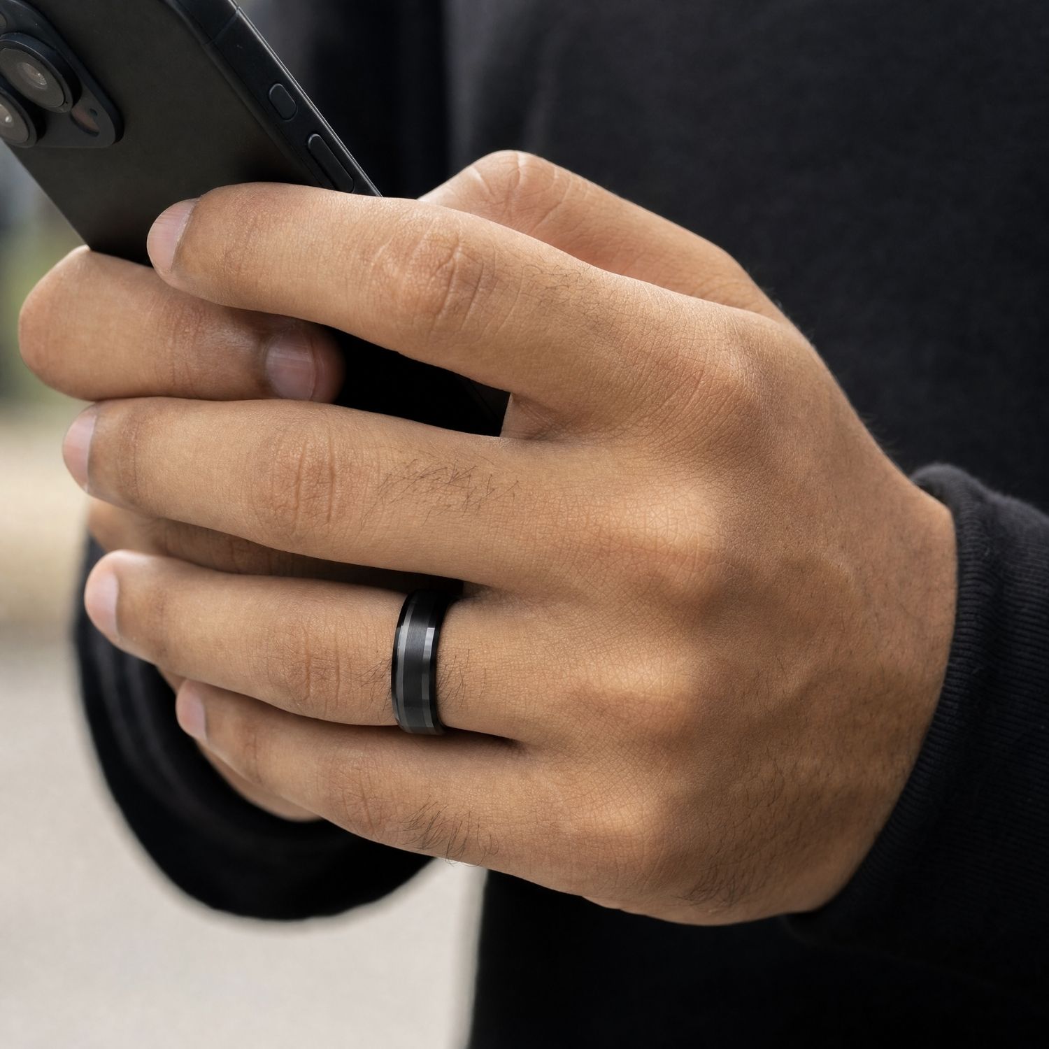 Close-up of a man's hand holding his phone while wearing the Spirit black tungsten ring, showing its brushed centre and polished bevelled edges.