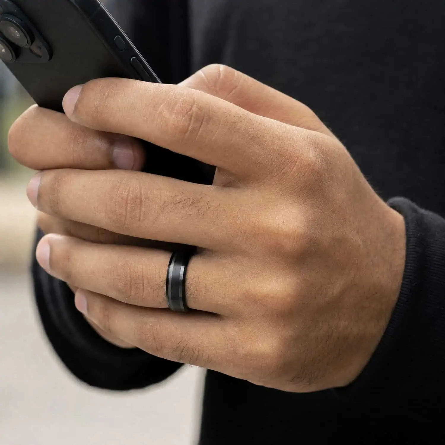 Close-up of a man's hand holding his phone while wearing the Spirit black tungsten ring, showing its brushed centre and polished bevelled edges.
