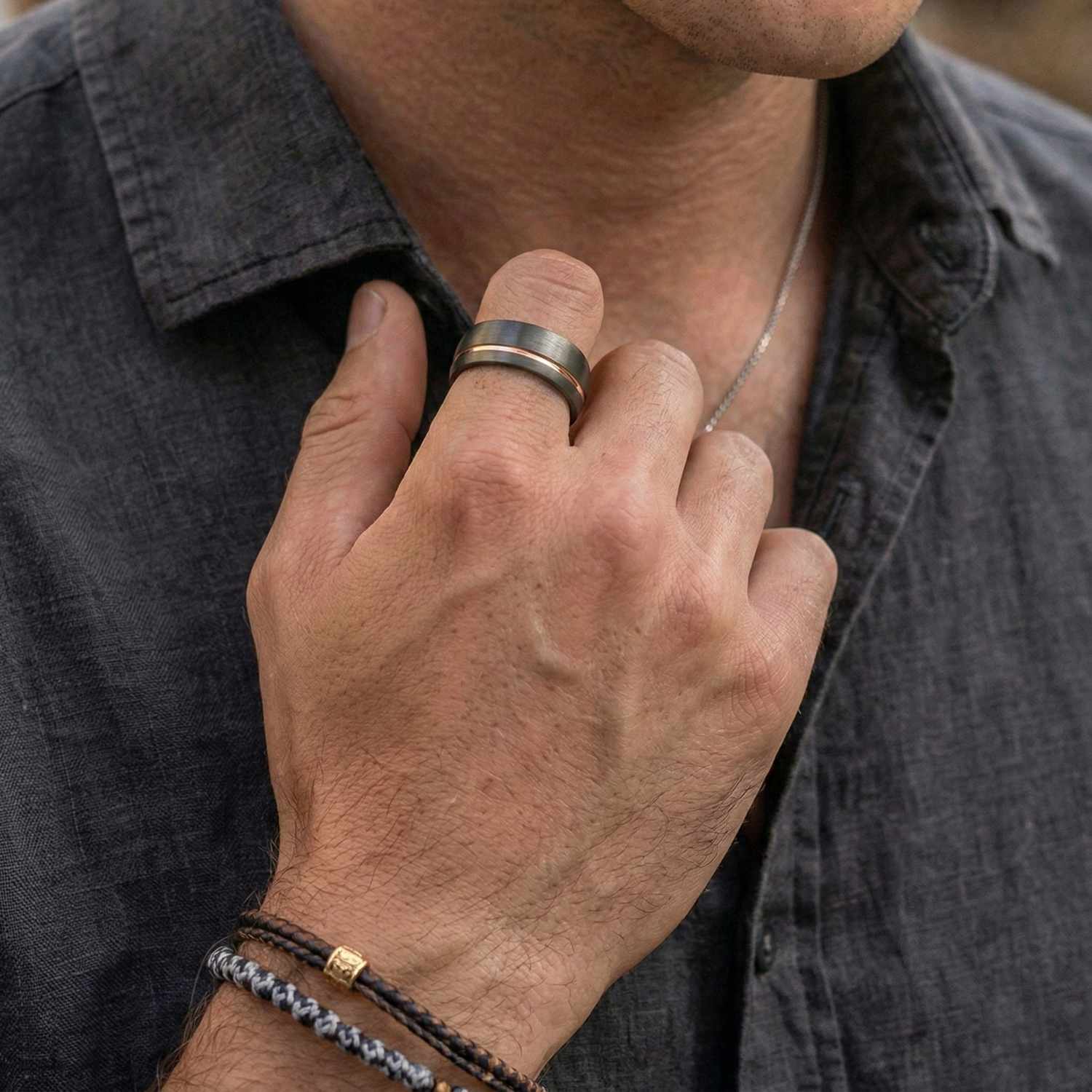 A mean reaches up to straighten his colour. He wears two bracelets on his wrist and is wearing a tungsten ring. Gunmetal grey in colour, the ring features a groove of rose gold, and is rose gold on the inside.