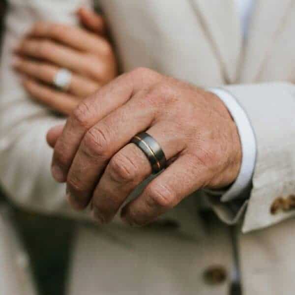 A close up of the newly married couple. Linking arms, you can see the new wedding rings. The woman has a shining silver ring while the man wears a tungsten grey ring with a rose gold groove that is slightly off centre. The inside of the ring is also rose gold.
