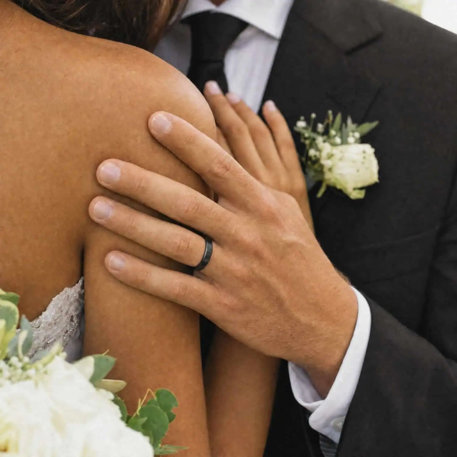 Bride and groom standing together with the groom's hand resting on his bride's shoulder while wearing the Raven thin black titanium wedding band.