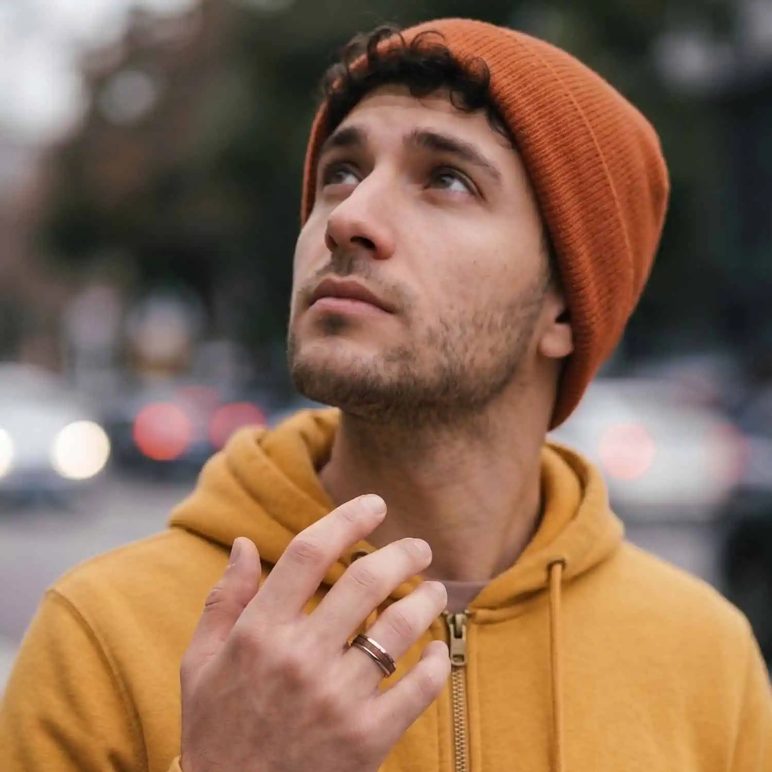 Man wearing a yellow hoodie and beanie walking through the city while wearing the Woodrow men's silver tungsten ring with a natural wood inlay.
