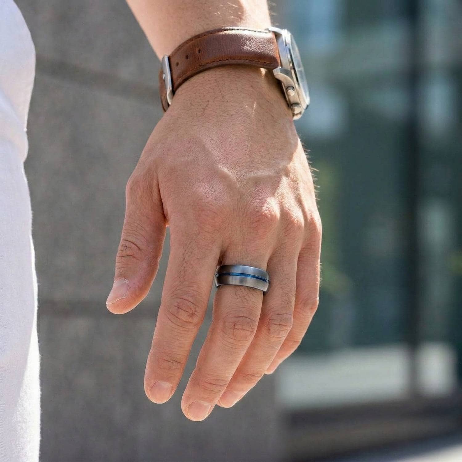 A close up image of a mans hand. One the middle finger, the man wears a ring. It is a gunmetal grey tungsten ring that has a groove of blue running through its centre.