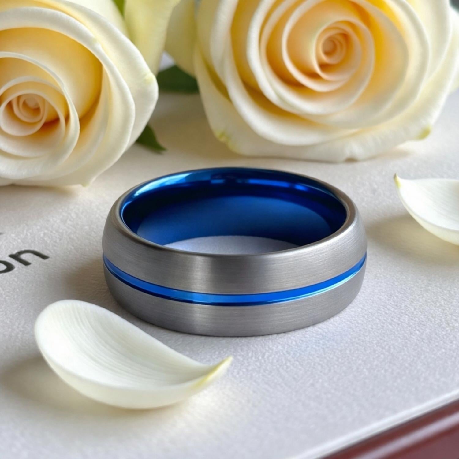 A stunning gunmetal grey tungsten ring sits amongst the cream wedding flowers. The ring has a brushed finish and a vibrant groove of blue runs through its centre.