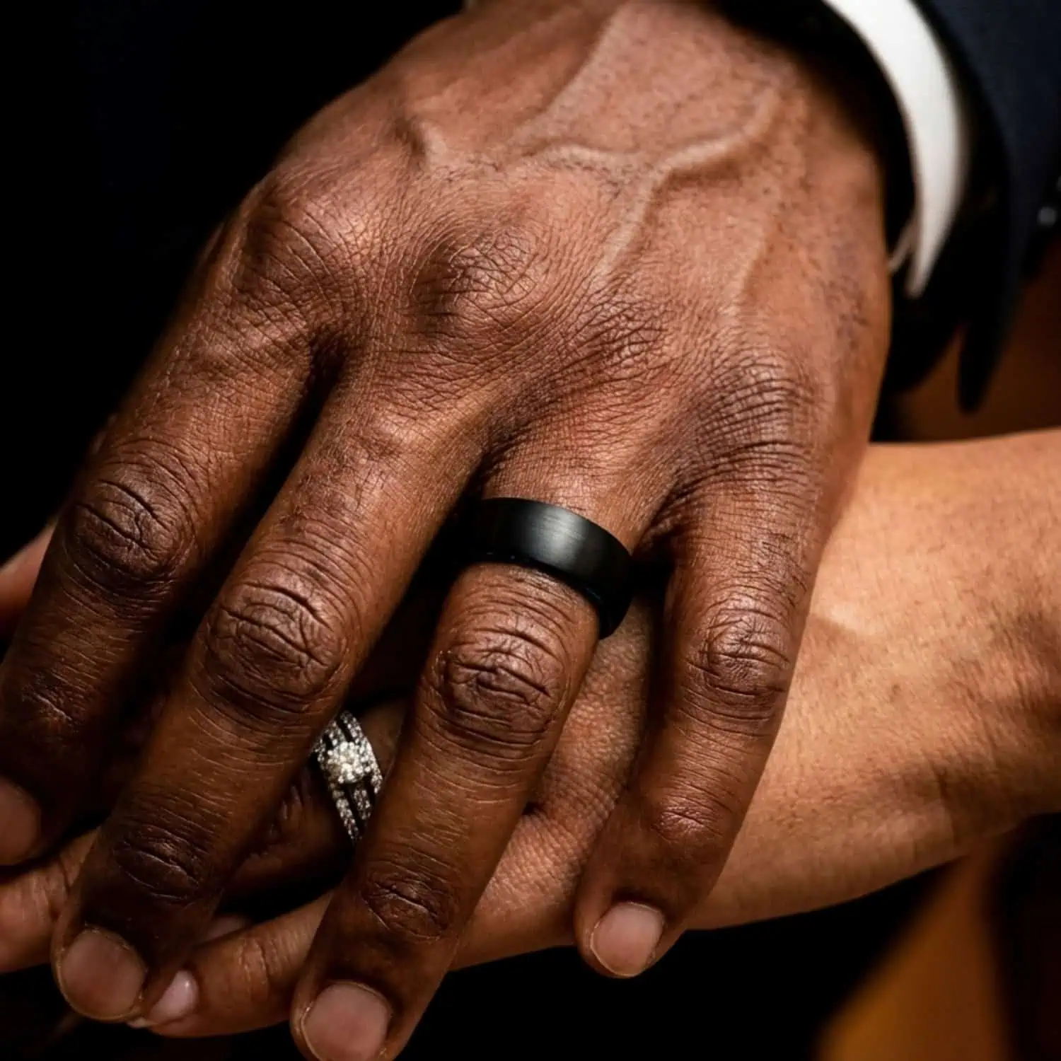 Close-up of newlyweds wearing their wedding bands as the groom rests his hand over his wife's while wearing the Valley brushed black tungsten wedding ring.