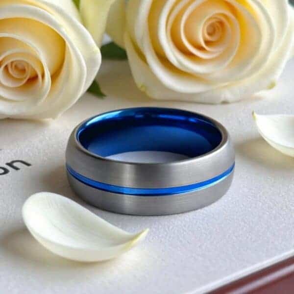 A stunning gunmetal grey tungsten ring sits amongst the cream wedding flowers. The ring has a brushed finish and a vibrant groove of blue runs through its centre.