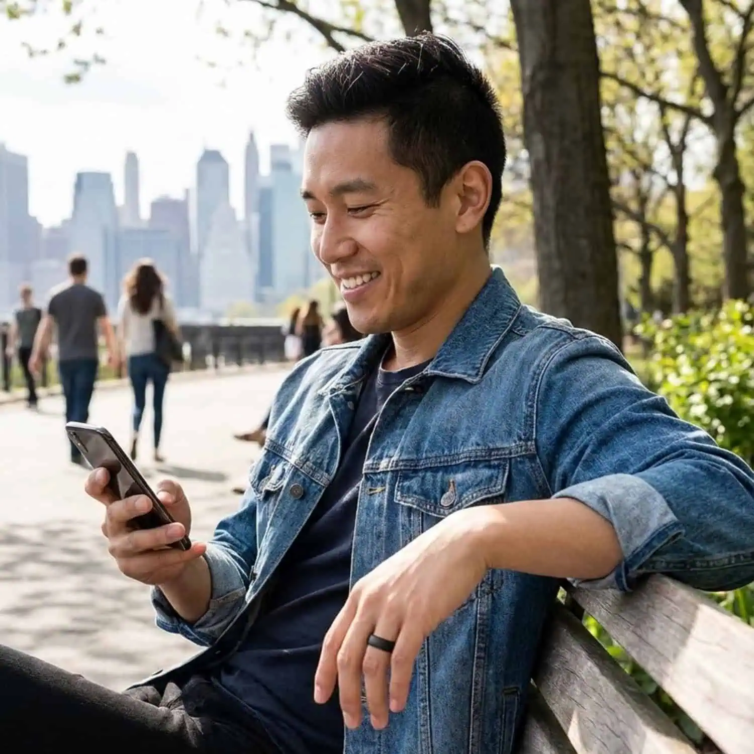 Man sitting in the sunshine on a park bench while looking at his phone and wearing the Valley brushed black tungsten ring.
