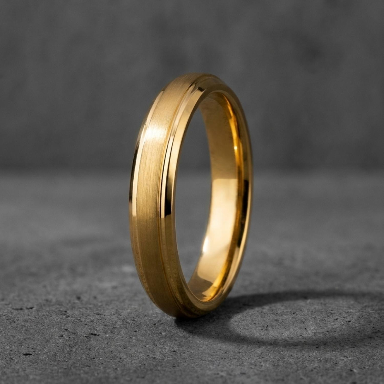 Close-up of the Eloquent Thin Style men's slim gold tungsten carbide ring standing upright against a minimalist grey background.