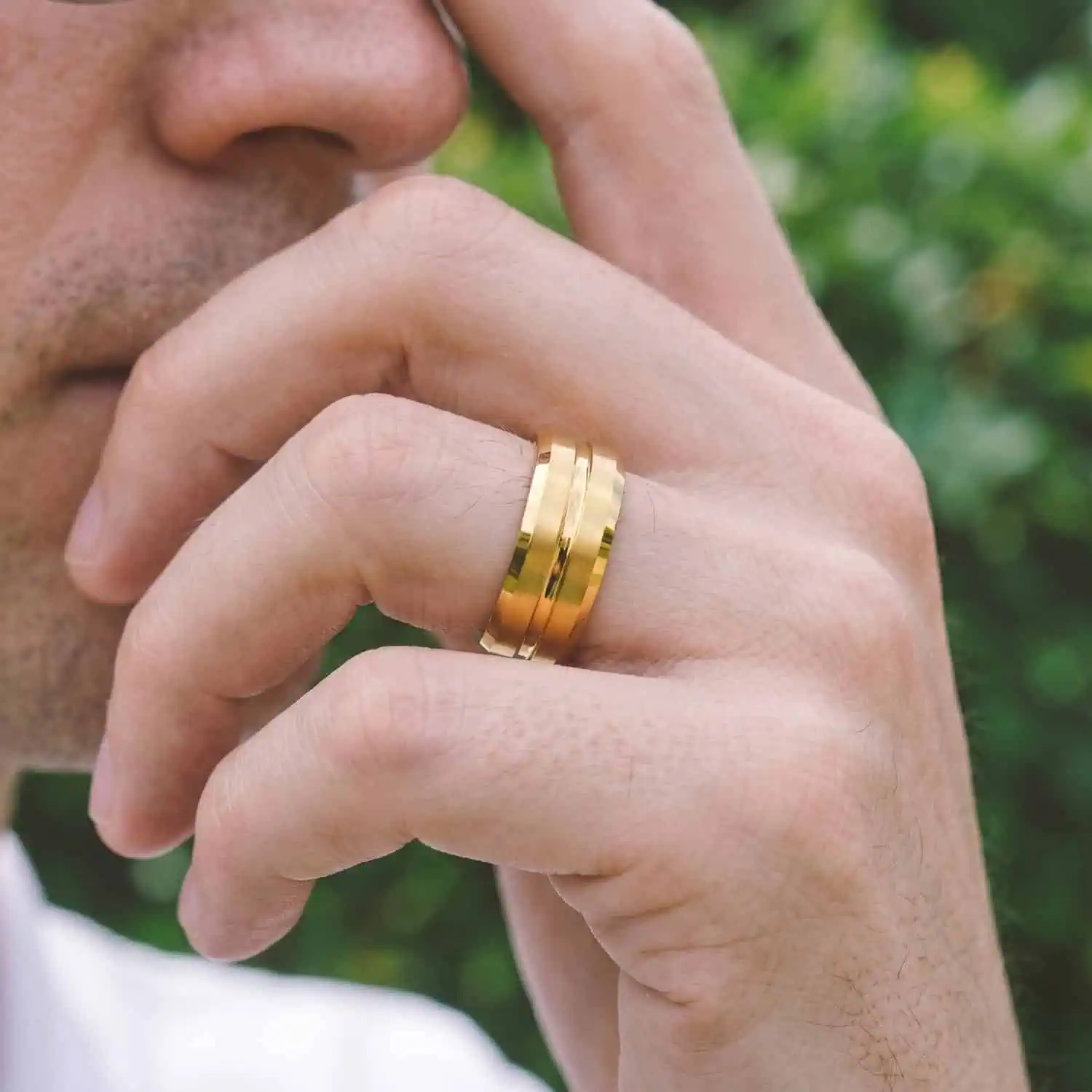 Thoughtful man wearing the Valour gold tungsten ring on his wedding finger, featuring brushed raised sections and a polished centre groove.
