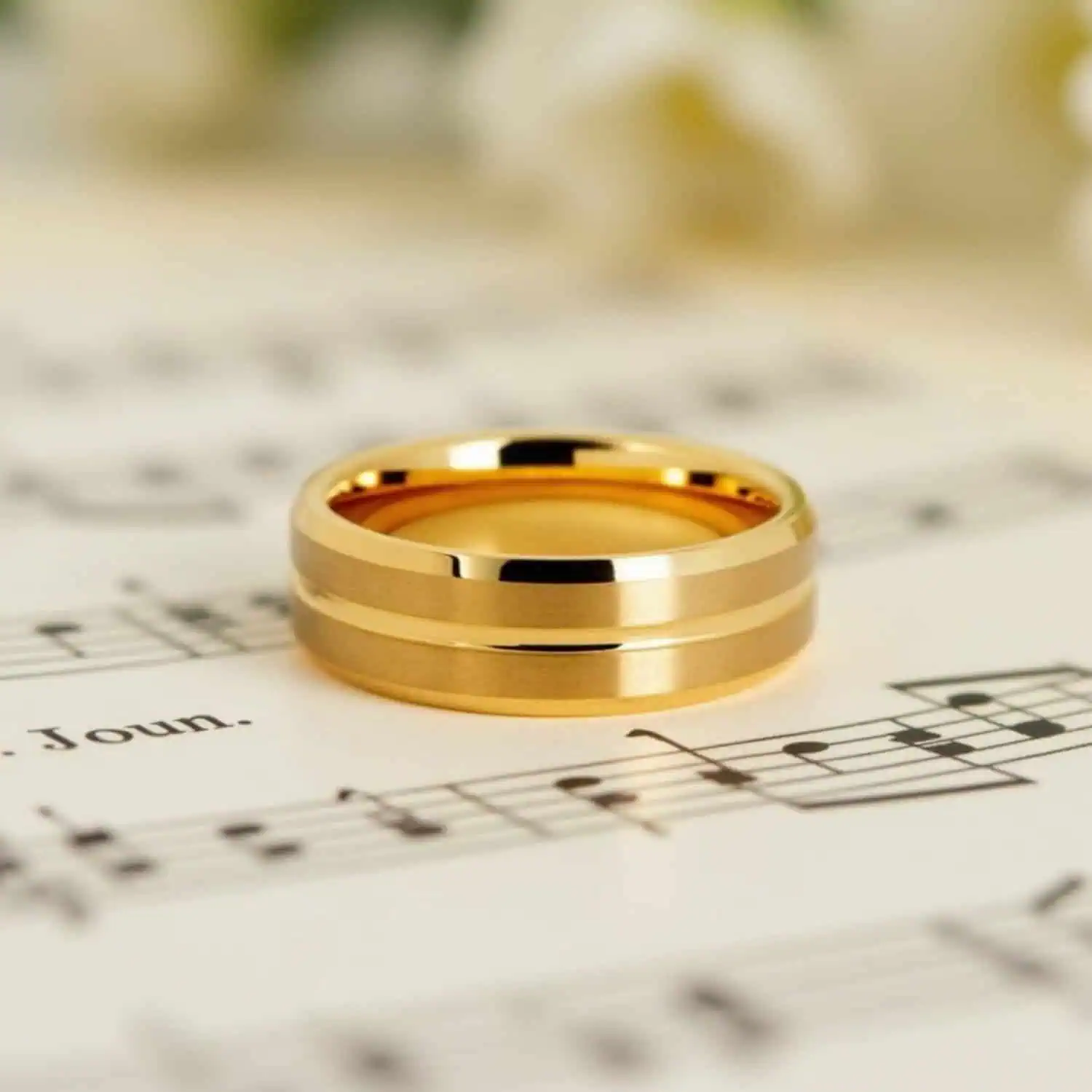 Front view of men's gold tungsten ring resting on sheet music, showcasing its brushed raised sections, polished centre groove, and polished bevelled edges.