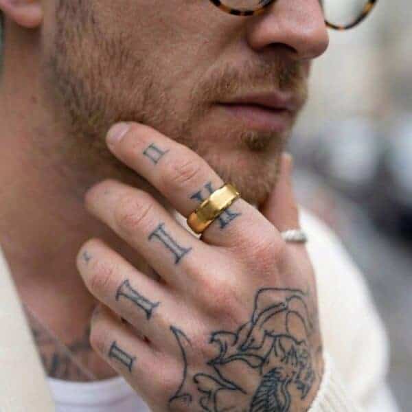 A man holds his hand to his chin. On his hand are many tattoos. He is wearing a gold tungsten ring. The centre of the ring is brushed and the edges are polished.