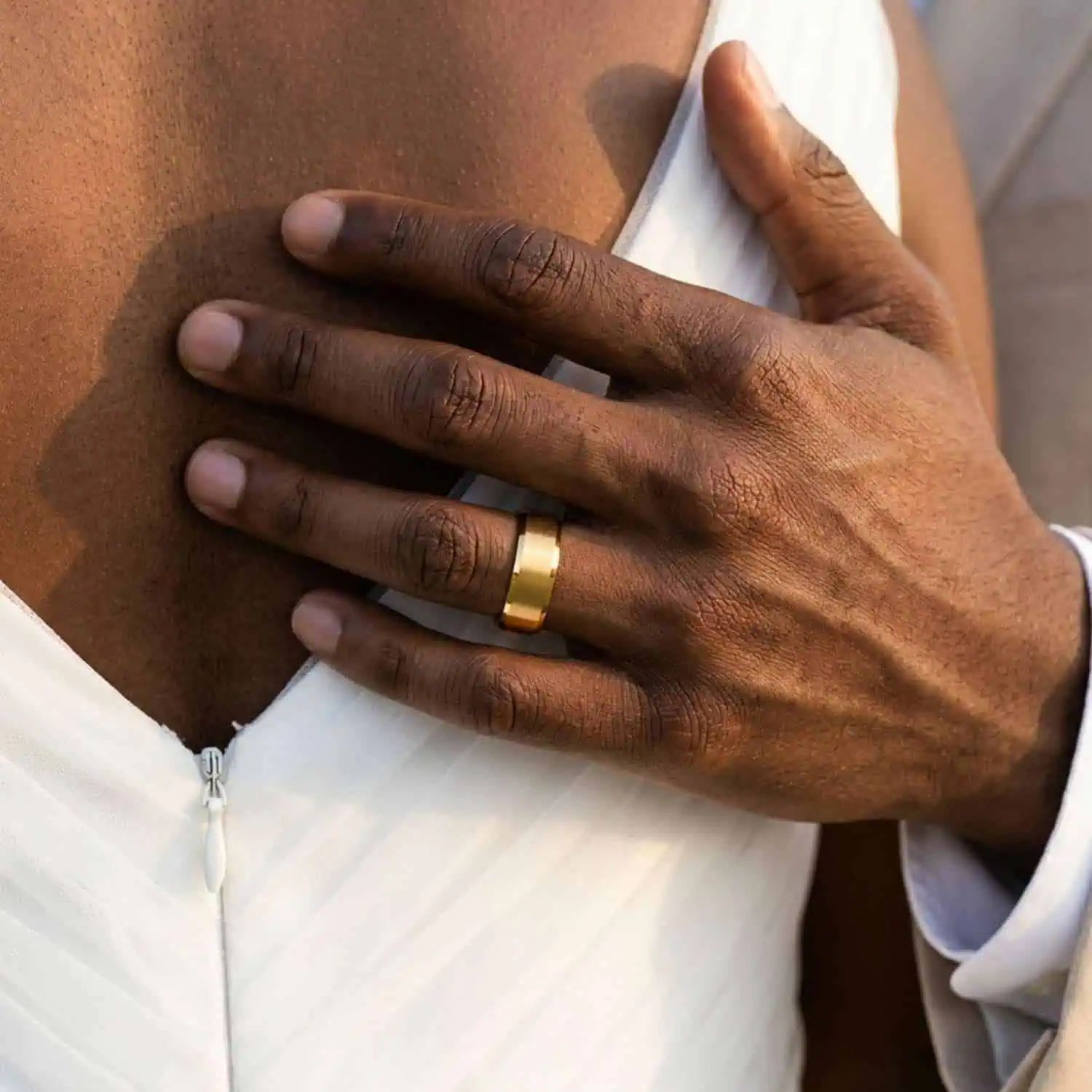 Newly married couple embracing as the groom wears the Regent brushed gold tungsten carbide wedding band with polished bevelled edges.