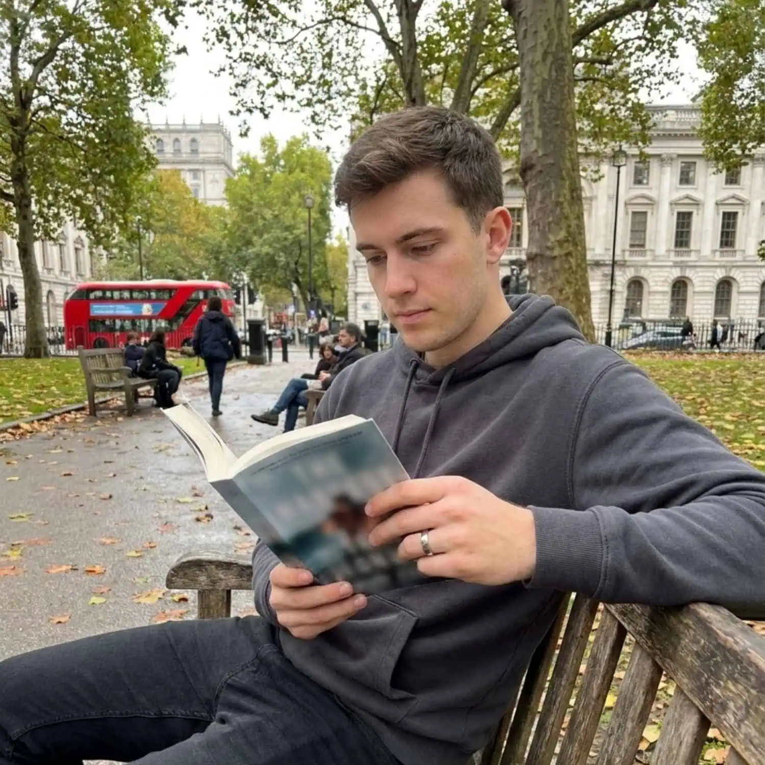 Man relaxing on a city park bench reading a book while wearing the Legacy polished white gold tungsten ring.