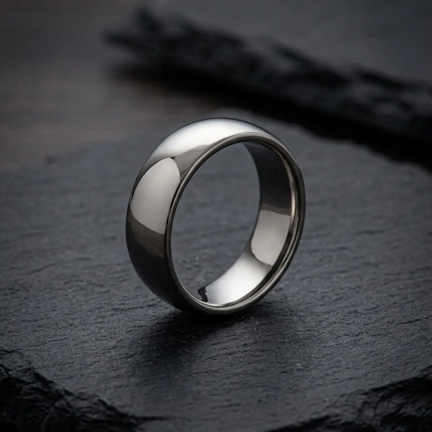 Legacy polished white gold tungsten ring standing upright on a charcoal slate surface, highlighting its bright polished finish and contemporary profile.