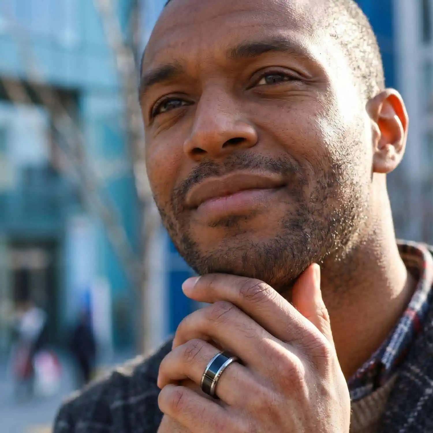 Smiling man outdoors with his hands clasped beneath his chin, wearing the Veritas polished silver tungsten ring with polished bevelled edges.