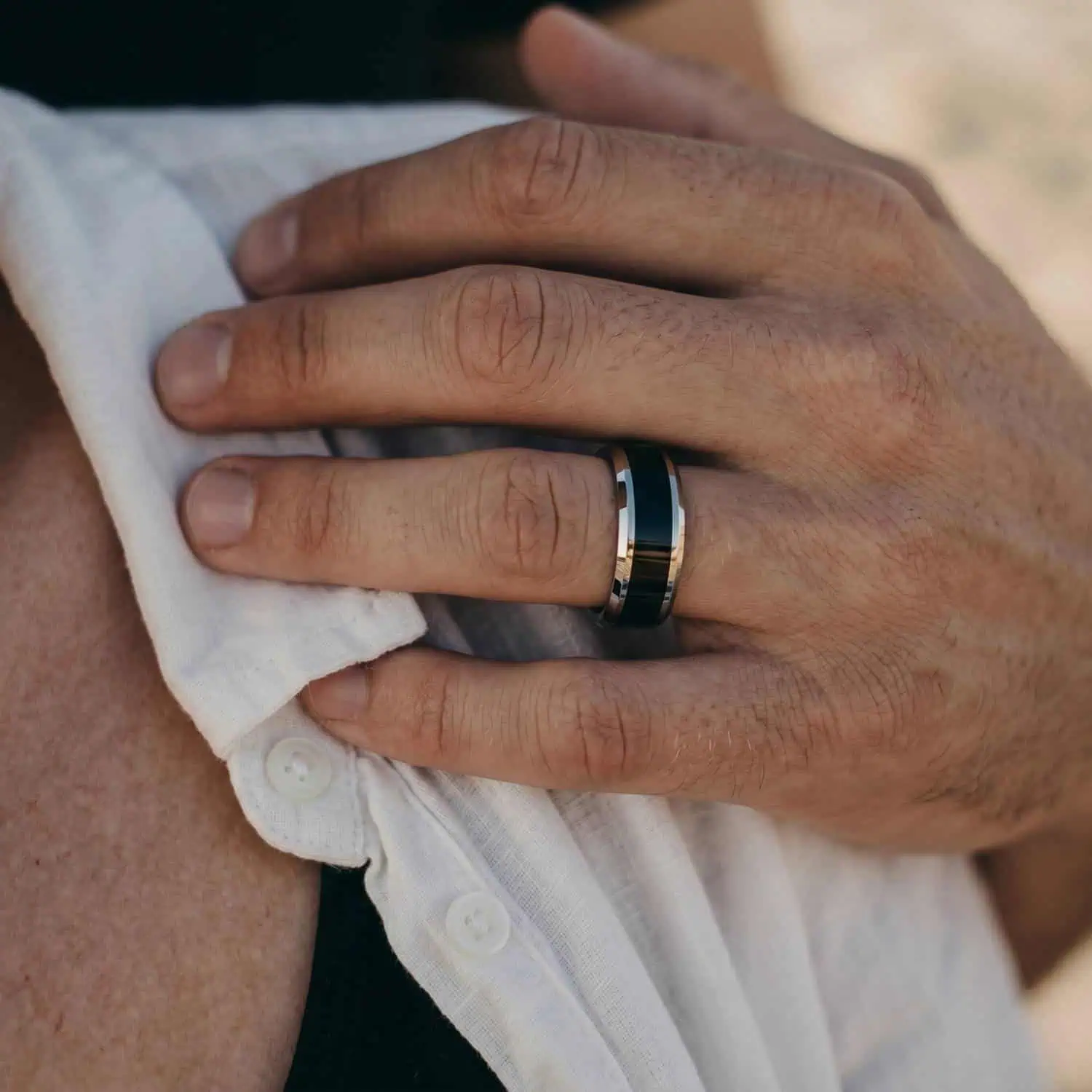 Detailed view of a man's hand wearing the Veritas tungsten ring while resting his hand on his partner's shoulder during a romantic moment.
